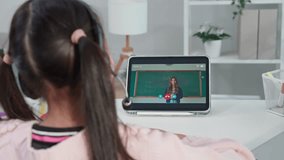 Rear view of young student learning online class with teacher at home. Adorable child student wearing headphones, using digital tablet study from school tutor by virtual remote online in living room. - Powered by Shutterstock - Get 15% off with code: PIKWIZARD15