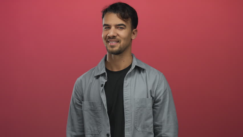 Young hispanic man giving thumbs up with a cheerful smile in front of an isolated red background showing a confident and positive gesture while wearing a casual shirt