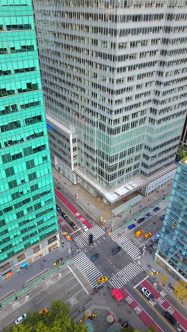 Aerial drone photo of busy Manhattan New York intersection surrounded by glass skyscrapers and green trees showing city traffic, yellow taxis, crosswalks and vibrant downtown architecture
