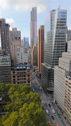 Aerial drone photo of Manhattan New York City shows tall modern skyscrapers, busy avenue and green park trees under bright daylight sky capturing city life and impressive urban architecture. New York.