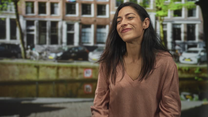 Woman smiling with clenched fists on street by building facade, visible face and hands; joy triumph.
