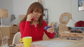 Senior woman in a living room makes a call holding a credit card surrounded by unpacked boxes symbolizing a new home transition and financial planning. - Powered by Shutterstock - Get 15% off with code: PIKWIZARD15