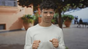 Man wearing glasses and white sweater squints eyes and clenches fists on crowded city street; discomfort. - Powered by Shutterstock - Get 15% off with code: PIKWIZARD15
