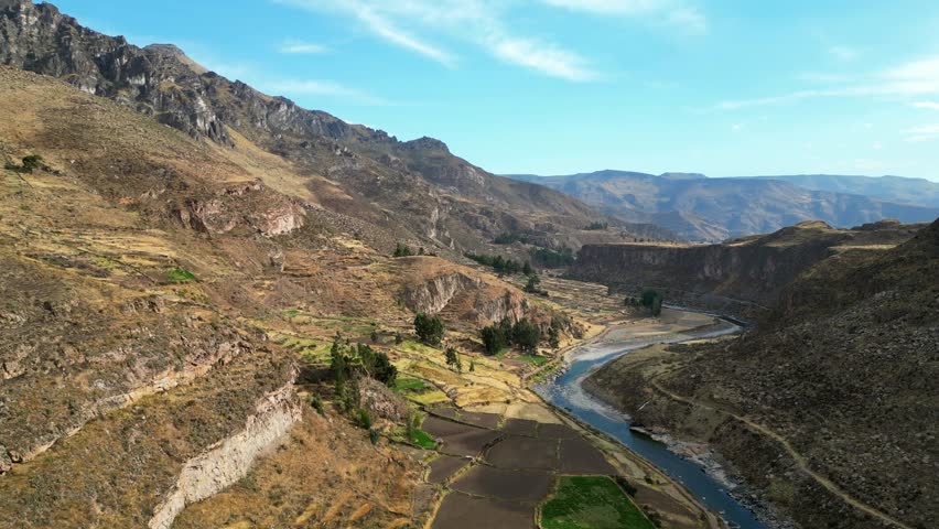 Aerial 4K shot of the Andes in Peru at sunrise, soft golden rays lighting up the valley floor and shimmering along a curving river.
