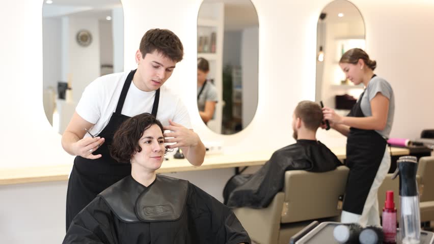 Male hairdresser stylist gives haircut to adult woman client in beauty salon