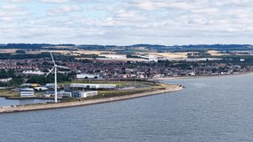 Drone pans over wind turbine, waterfront, and cityscape under bright daylight with scattered clouds - Powered by Shutterstock - Get 15% off with code: PIKWIZARD15