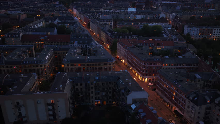Aerial drone view of long illuminated streets lined with historic Danish townhouses and apartments, glowing warmly as night falls in Copenhagen