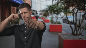 Man finger pointing at camera on city street near red planters and a parked car, rolled sleeves and casual black shirt; confidence. - Powered by Shutterstock - Get 15% off with code: PIKWIZARD15