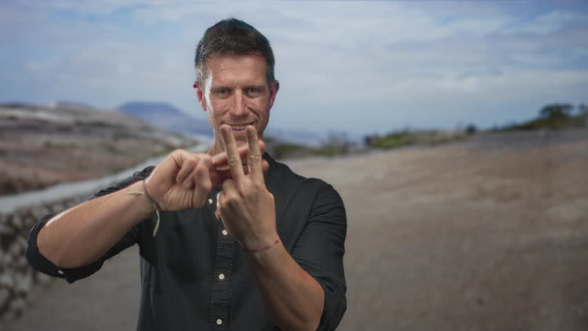 Man showing three fingers while counting on hands on a street path with stone wall; focus confidence.