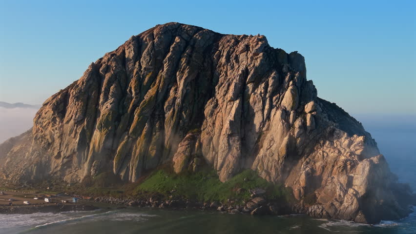 Scenic view of Morro Rock at Morro Bay California surrounded by gentle Pacific Ocean waves under clear blue sky capturing natural beauty, coastal landscape and famous California landmark