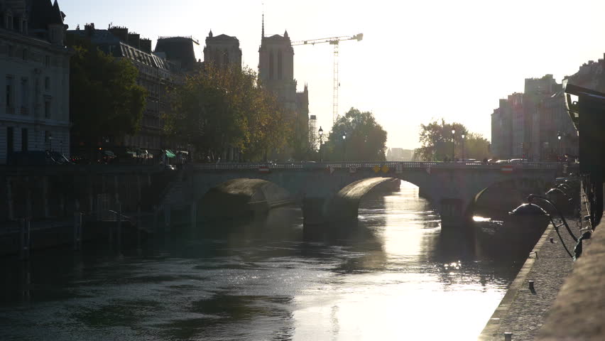 Golden hour view of Pont Saint-Michel bridge over the Seine River in Paris, with Notre-Dame Cathedral in the distance. Warm sunlight reflects on the water, highlighting the charm and architecture