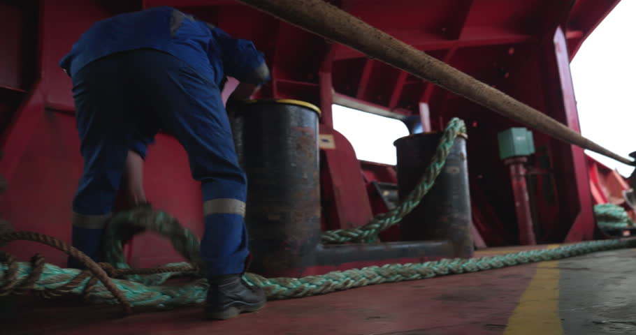 Skilled worker in uniform unties cable from metal supports in vessel dock closeup. Employee unmoors large tanker working with cable in port