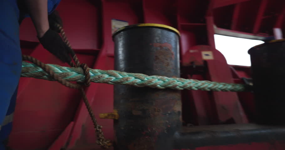 Worker in uniform coils thin cable onto rope on ship vessel deck closeup. Employee ties fastening of tanker mooring during marine sailing