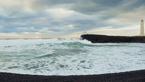 Dramatic footage of powerful waves rolling onto a volcanic black sand beach in Iceland. The scene features a rugged coastline, a dark cliff, and a prominent lighthouse standing on the shore under a cl - Powered by Shutterstock - Get 15% off with code: PIKWIZARD15