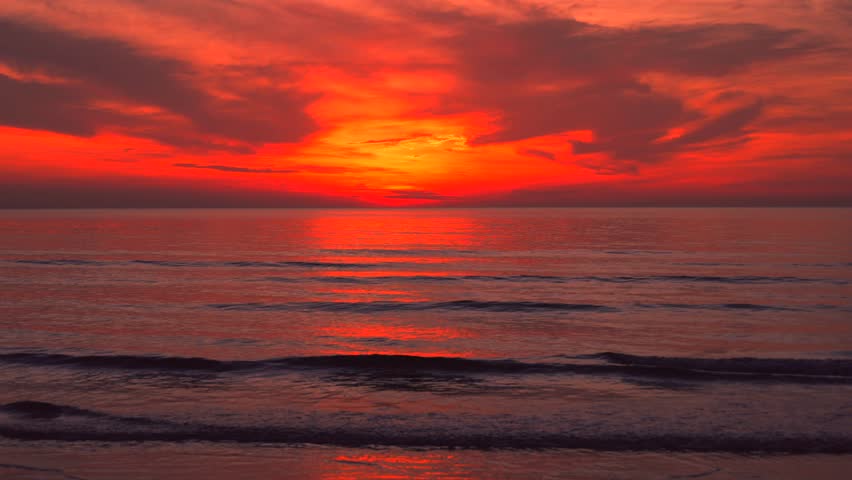 Tropical time before sunrise seascape with glowing red clouds above calm ocean water