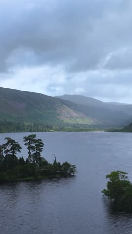 Slow panoramic movement across tranquil lake, forested island, and misty mountains under overcast sky