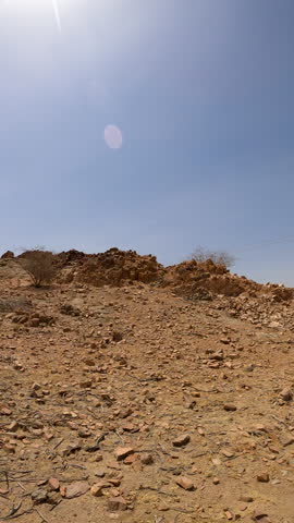 A sun-baked, rocky desert landscape with scattered twigs, arid mountain slopes, and rugged hills under a clear blue sky—perfect for travel, nature, adventure, geology, or environmental B-roll footage.