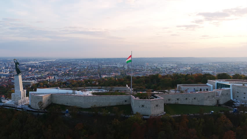 Citadella fortress on Gellért Hill with the Liberty Statue and Hungarian flag overlooking Budapest at sunset.