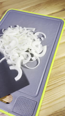 Vertical video - Closeup dolly shot of a sliced white onion next to a bladed cutting tool, on a chopping board.