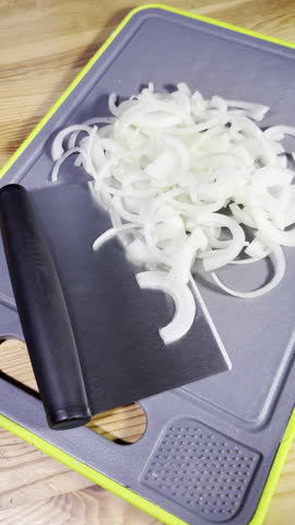 Vertical video - Closeup dolly shot of a sliced white onion next to a bladed cutting tool, on a chopping board.