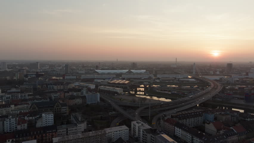 Panoramic aerial view of cityscape of Mannheim, Germany. Cars drive on a complex highway interchange with Neckar river at sunset