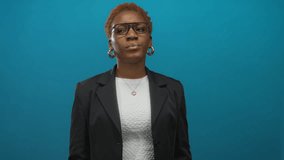 Woman wearing glasses and black blazer clutching shoulder in blue studio set with closed eyes and tense expression; discomfort. - Powered by Shutterstock - Get 15% off with code: PIKWIZARD15