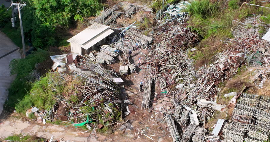 In this sprawling yard, amid a chaotic jumble of metal poles and scaffolding, several workers are actively moving long bamboo rods.