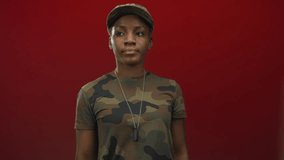 Young african american woman in camouflage uniform and cap salutes with dog tag in studio; pride duty honor strength. - Powered by Shutterstock - Get 15% off with code: PIKWIZARD15