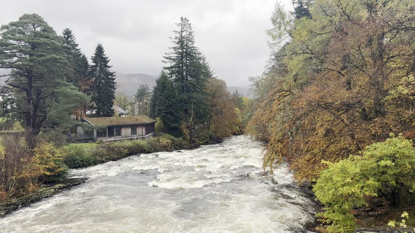 Looking across the rushing waters of the Falls of Dochart in the Scottish Highlands. The trees are boasting a stunning array of Autumn colours.