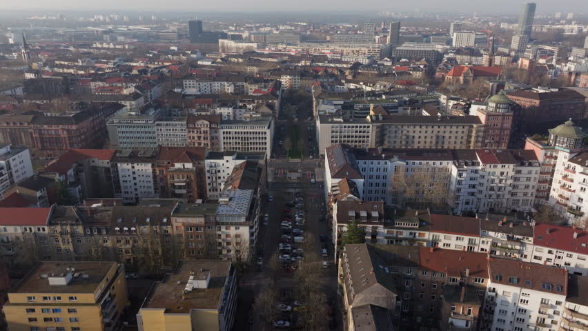 Aerial view flying above long, straight road surrounded by historic buildings and apartment blocks in city of Mannheim, Germany