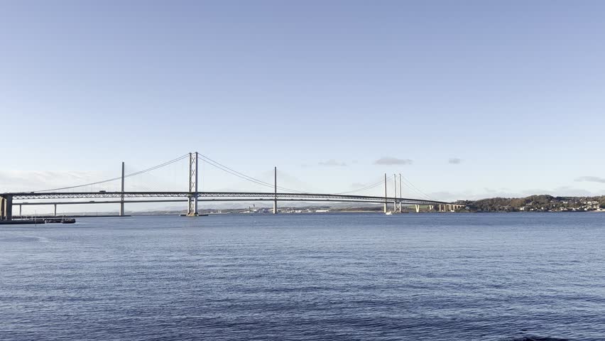 Looking across the First of Forth from Queensferry towards the Forth Road Bridge and the Queensferry Crossing. The bridges are set against a clear blue sky above.