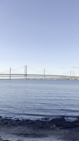 Looking across the First of Forth from Queensferry towards the Forth Road Bridge and the Queensferry Crossing. The bridges are set against a clear blue sky above.