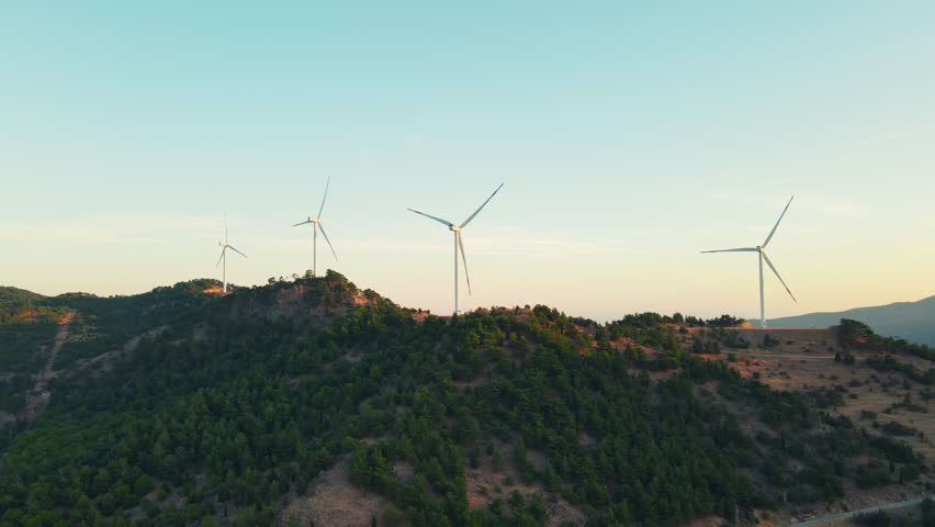 Wind turbines above rolling hills in soft morning haze, aerial view. Wind energy deployment contributes to net-zero electricity