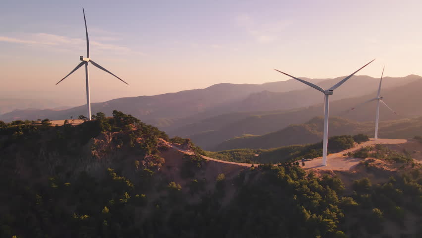 Wind turbines spaced across hilly ridges in sunrise haze, aerial view. Net-zero supported by renewable wind resources