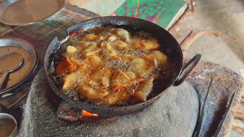 Golden samosas frying in bubbling oil on a traditional clay stove, creating a rustic Indian street food scene with rich aroma and sizzling texture.