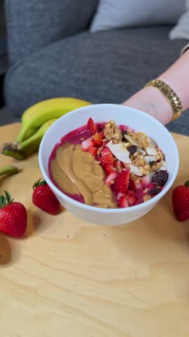 hand presenting a thick acai smoothie bowl topped with peanut butter, strawberries, granola, and coconut—clean vertical b-roll ideal for recipe videos, wellness ads, and breakfast.
