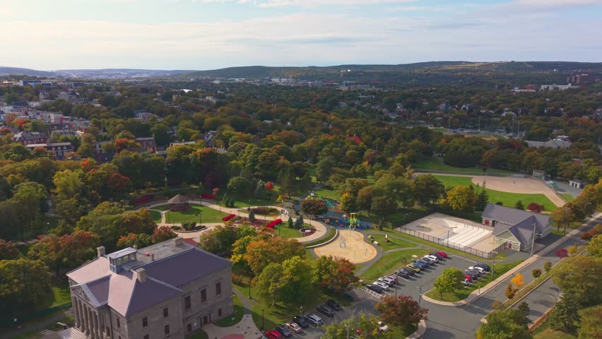 Urban aerial of St. John’s park with figure‑eight path, playground and autumn trees; Victorian homes and skyline frame the greenery.