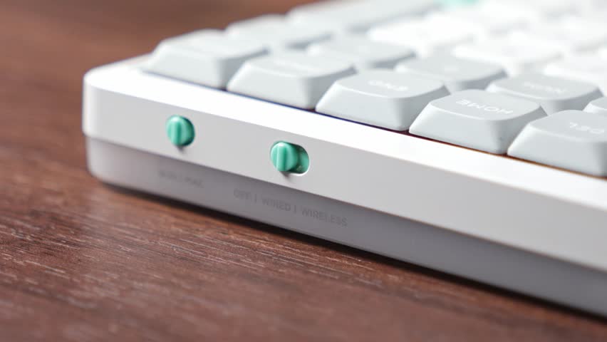 Finger operates a green switch on a white mechanical keyboard, enabling selection between WIRED WIRELESS modes, offering versatile, efficient connection for any digital task