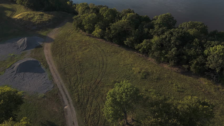 Drone tilts up over dirt path to reveal Neosho River and Lake Hudson near Kerr Dam, Oklahoma