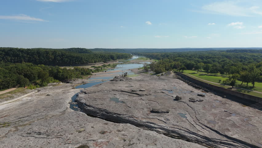 Rocky layered terrain and exposed riverbed upstream from Pensacola Dam in Oklahoma, aerial orbit tilt down