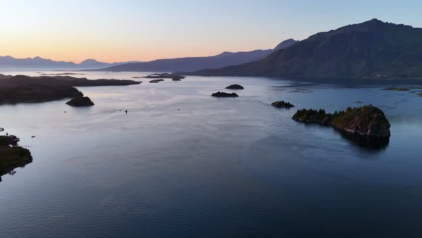 An aerial view revealing the serene, dark waters of Raftsundet fjord in Lofoten, Norway, dotted with rocky islets and misty peaks at dusk