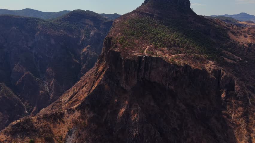 Steep rocky mountain cliffs with sparse trees under a bright sky and layered canyon formations