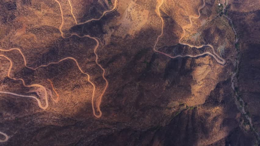 A Top-down view of winding mountain roads creating abstract curves across a dry rocky landscape