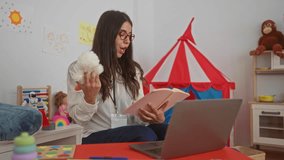 Hispanic woman teacher reading to preschool children in a vibrant kindergarten setting with toys tent and laptop - Powered by Shutterstock - Get 15% off with code: PIKWIZARD15