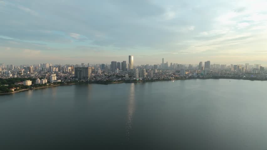 Morning panoramic view of West Lake with Hanoi skyline under soft clouds and calm water.