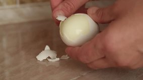 Woman peeling boiled egg with hands on kitchen table. Close-up of female hands peeling shell from a hard-boiled egg. Simple home cooking process, breakfast preparation, and healthy eating concept. - Powered by Shutterstock - Get 15% off with code: PIKWIZARD15
