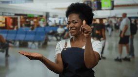 Woman in apron standing in airport terminal pointing at her palm with finger, surrounded by busy indoor setting, conveying professional but casual interaction. - Powered by Shutterstock - Get 15% off with code: PIKWIZARD15