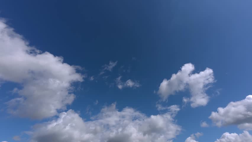 Wide timelapse showing cumulus clouds moving rapidly across bright blue sky on clear day. Atmospheric weather motion.
