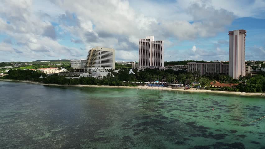 Scenic aerial view of Pacific Islands Club Guam Resort Hotel with lush greenery and stunning reef shoreline during daytime.
