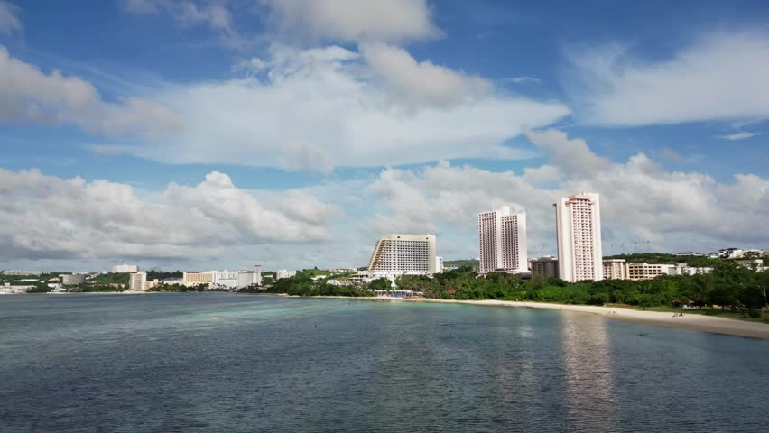 Picturesque aerial hyperlapse of moving clouds over crystal clear ocean waters and hotel resort buildings at Tumon Bay, Guam, USA.